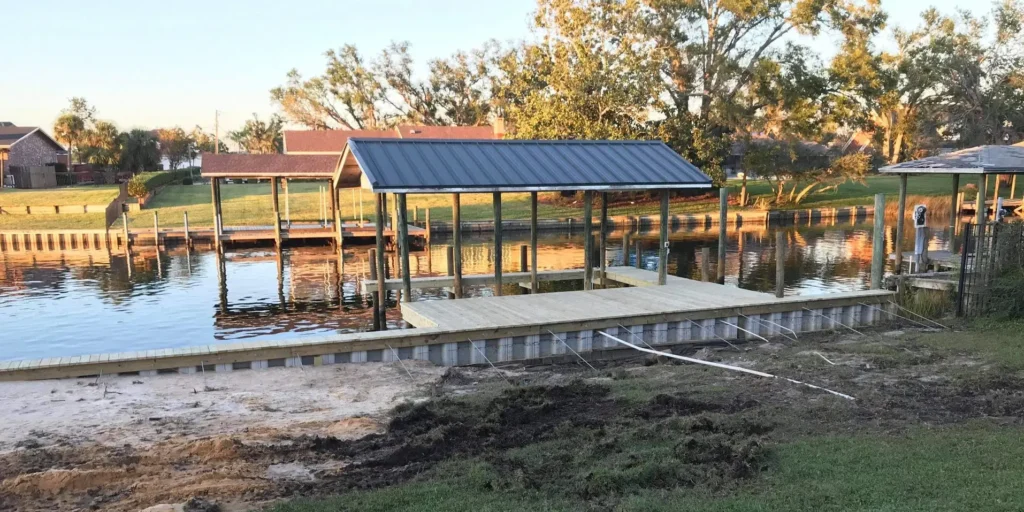 A repaired seawall with a wooden dock and covered structure along a canal, surrounded by grass and waterfront properties.