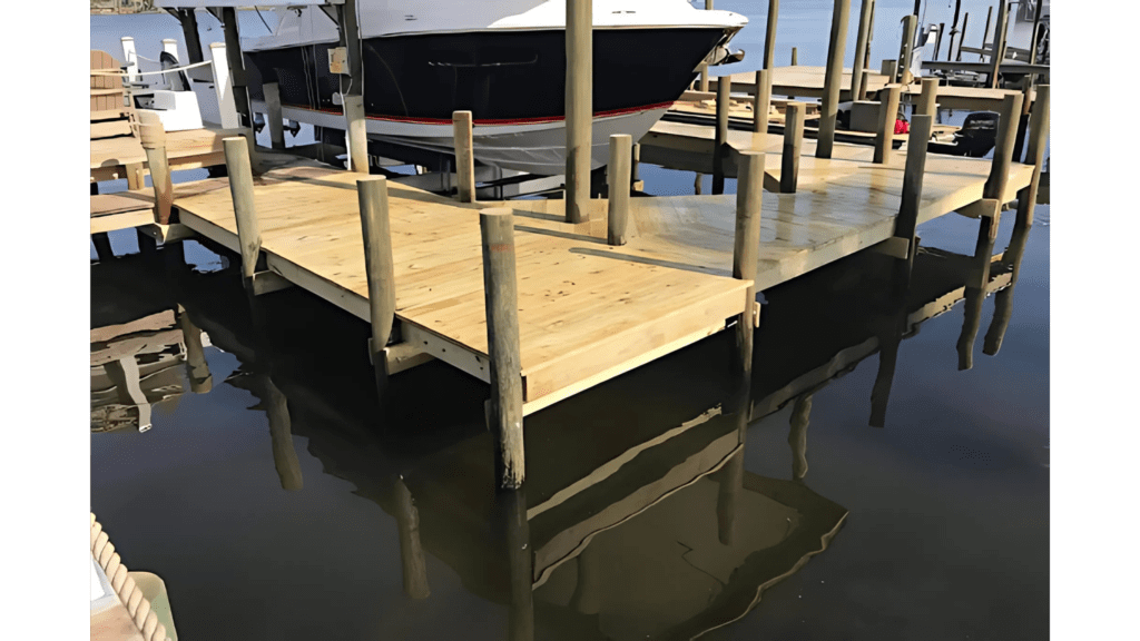 Wooden boat dock with multiple pilings extending over calm water, with a docked boat visible in the background.