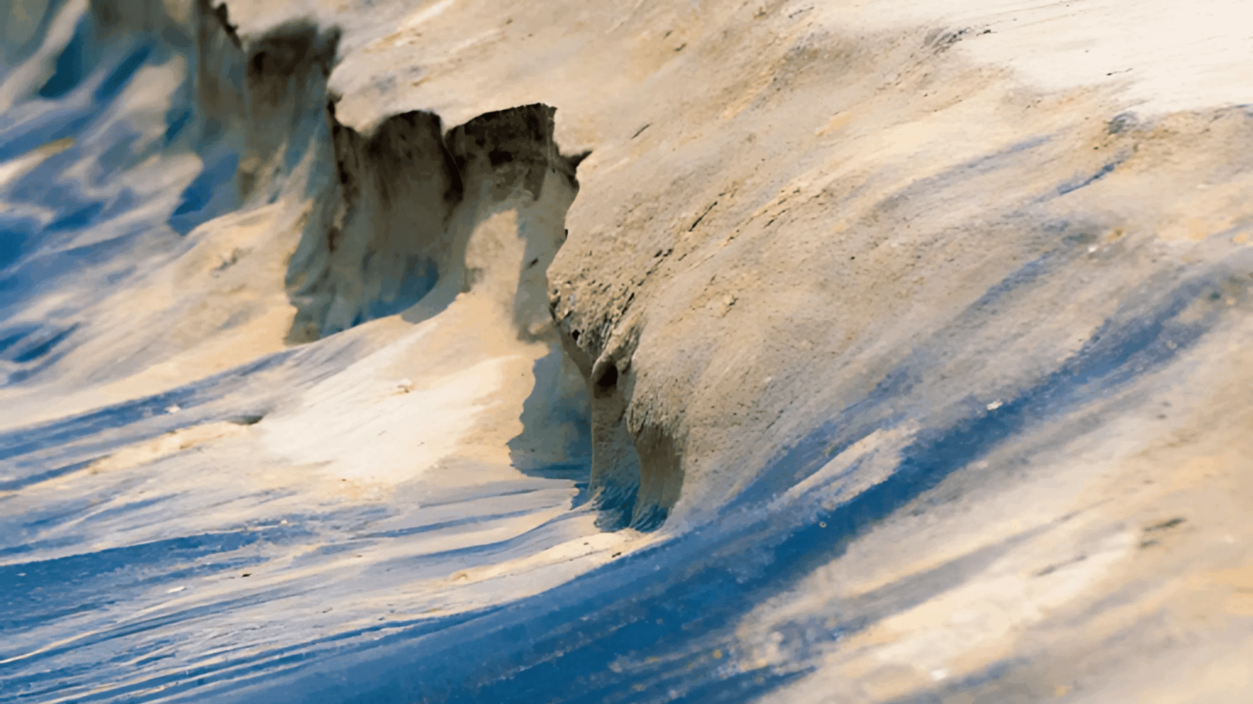 Close-up of eroded sand formations with layered textures in shades of beige and blue, shaped by wind and water.