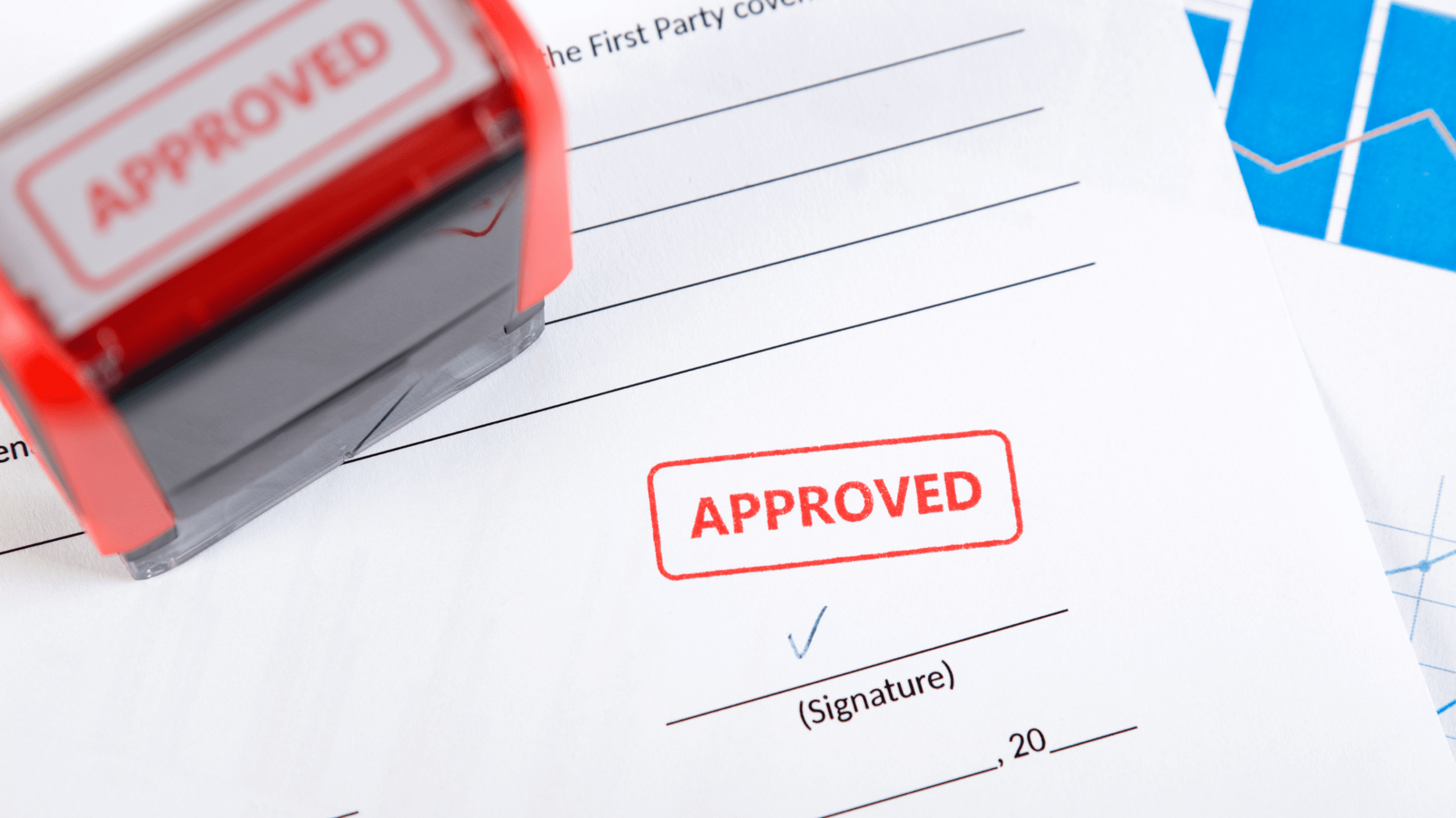 A red stamp marks a document as approved, with a signature line below. A stamp device and financial charts are visible nearby.
