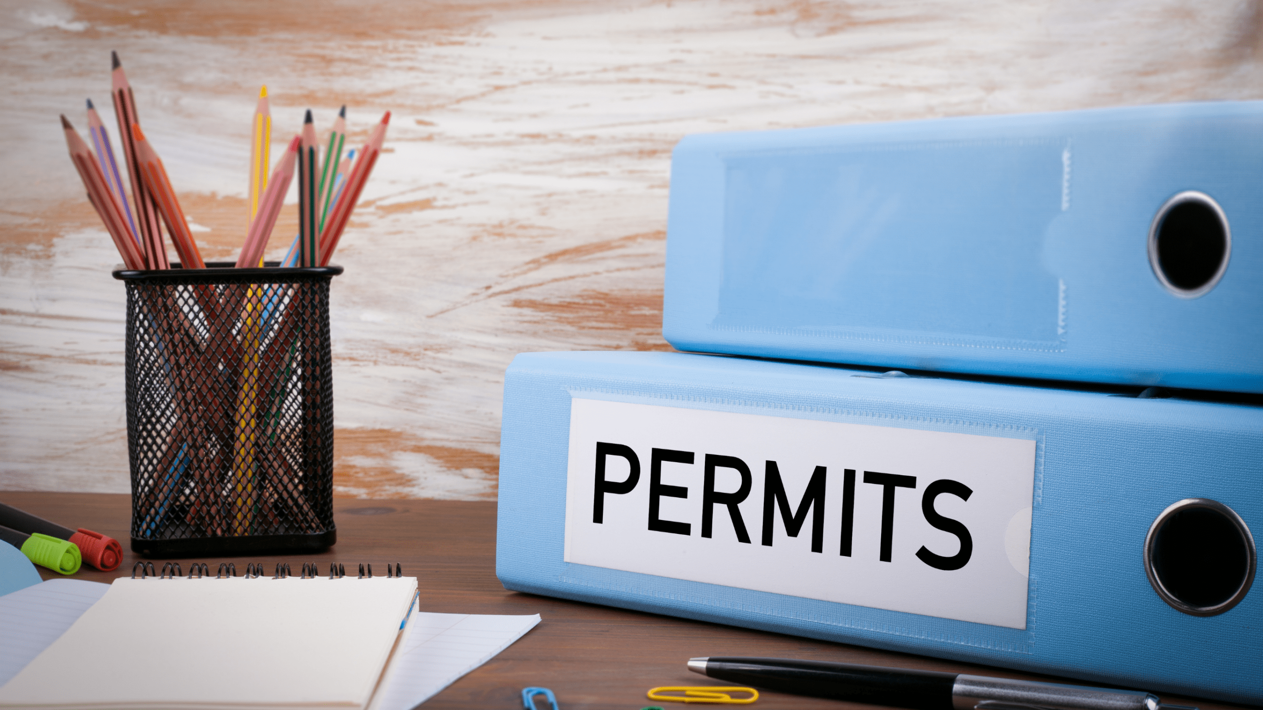 Two blue binders labeled permits sit on a desk with office supplies, symbolizing the paperwork required for a retaining wall permit.