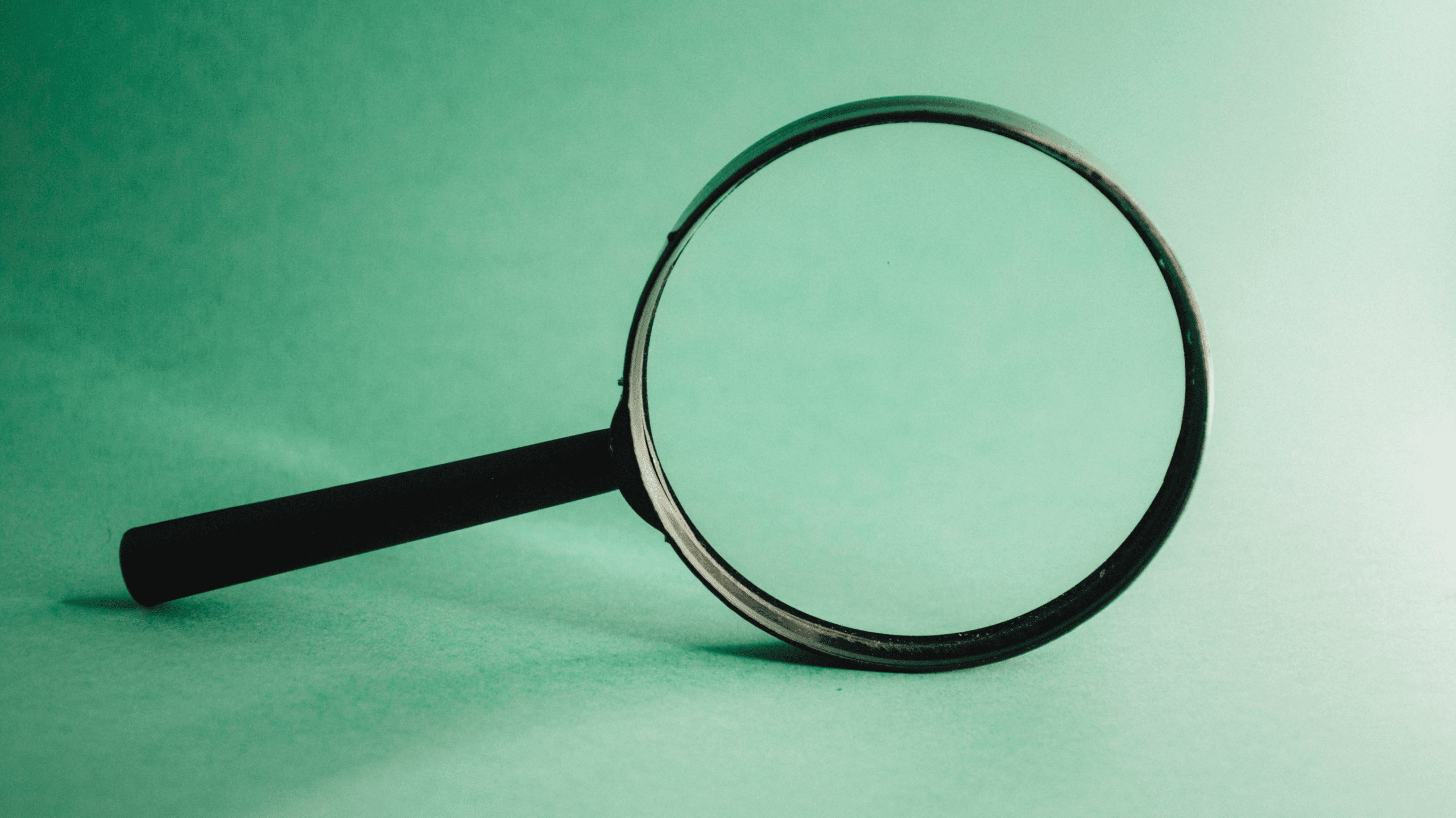 A black-handled magnifying glass lies on a green surface, symbolizing close examination, investigation, or a search for information.