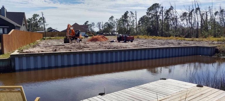 A newly constructed steel seawall along a waterfront property with an excavator and construction materials on-site for land development.