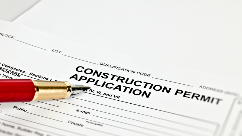 A close-up of a construction permit application form with a red and gold fountain pen resting on it, ready for completion.